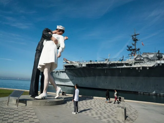 Groot standbeeld van een zoenende matroos en verpleegster op de kade, met het vliegdekschip USS Midway op de achtergrond in San Diego