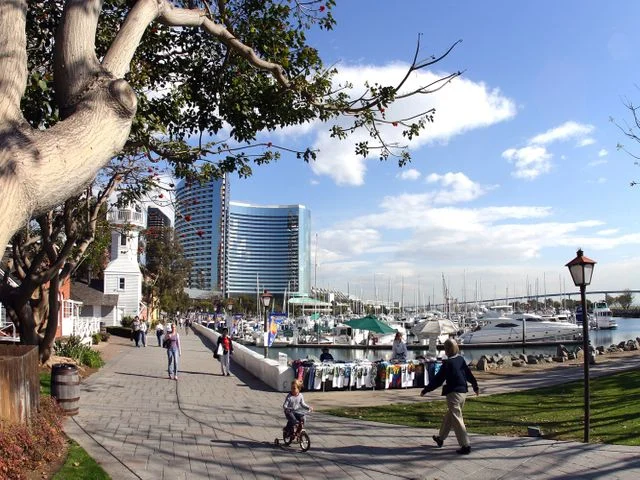 Wandelaars lopen over een boulevard langs een jachthaven met witte boten en hoge gebouwen in San Diego