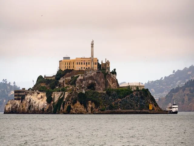 Voormalig gevangeniseiland Alcatraz met zijn gebouwen op de rotsen, met een boot die passeert in de baai van San Francisco