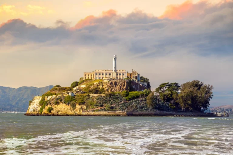 Uitzicht over de golvende baai op het rotsachtige Alcatraz Island met de vuurtoren en oude gevangenisgebouwen bij zonsondergang