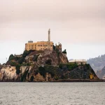 Het rotsachtige eiland Alcatraz met het oude gevangenisgebouw, gezien vanaf het water in San Francisco terwijl een boot voorbijvaart