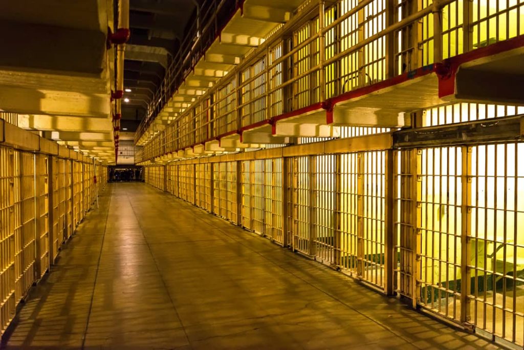 Lange gang tussen twee rijen cellen met gele tralies en warme verlichting in de voormalige gevangenis Alcatraz