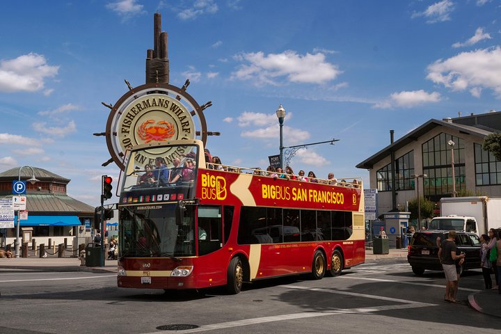 Rode dubbeldekker toeristenbus rijdt onder het scheepswiel bord van Fisherman's Wharf in San Francisco