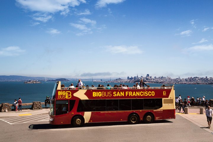 Rode dubbeldekker toeristenbus staat geparkeerd bij een uitkijkpunt met de baai en skyline van San Francisco op de achtergrond