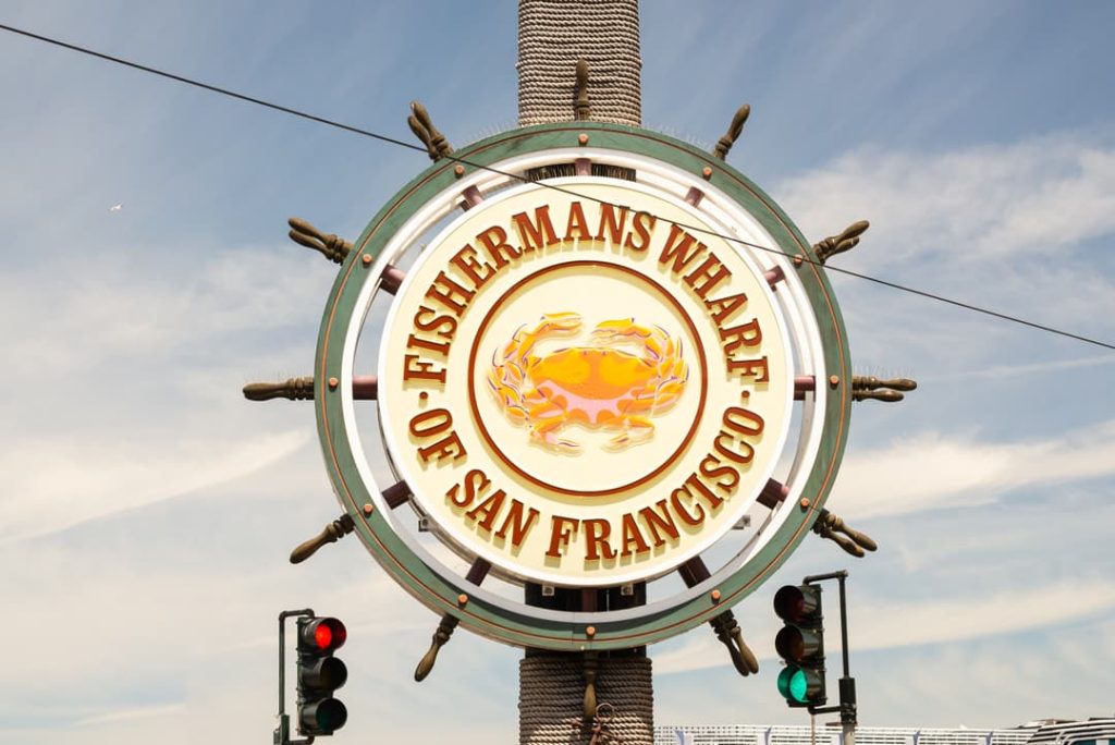 Rond metalen uithangbord met een krab in het midden en de tekst Fisherman's Wharf of San Francisco tegen een blauwe lucht