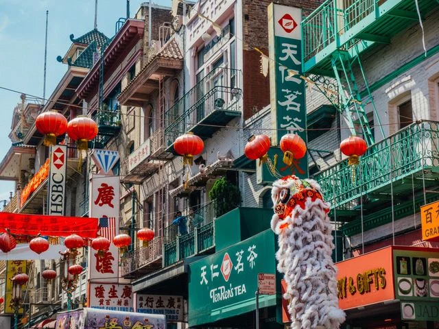 Rode lampionnen hangen boven een straat met winkels in Chinatown, met een drakendanser op de voorgrond in San Francisco