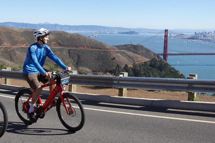 Man op een rode elektrische fiets rijdt over een heuvelweg met uitzicht op de Golden Gate Bridge en San Francisco