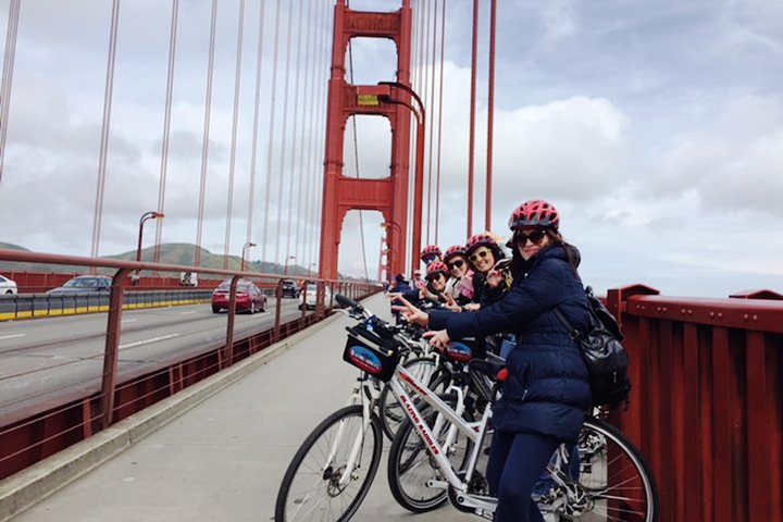 Groep fietsers met helmen poseert op het fietspad van de rode Golden Gate Bridge met verkeer op de weg ernaast