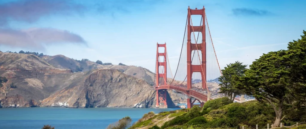 De rode Golden Gate Bridge over de baai, met groene heuvels en bomen op de voorgrond in San Francisco