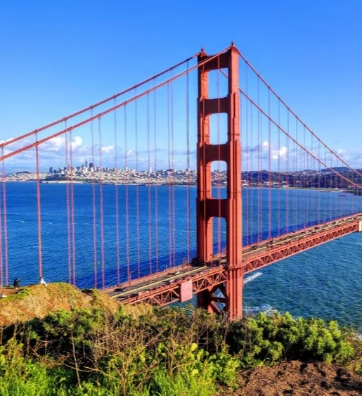 De rode Golden Gate Bridge met zijn hoge pyloon overspant de baai van San Francisco onder een strakblauwe hemel, met de skyline op de achtergrond
