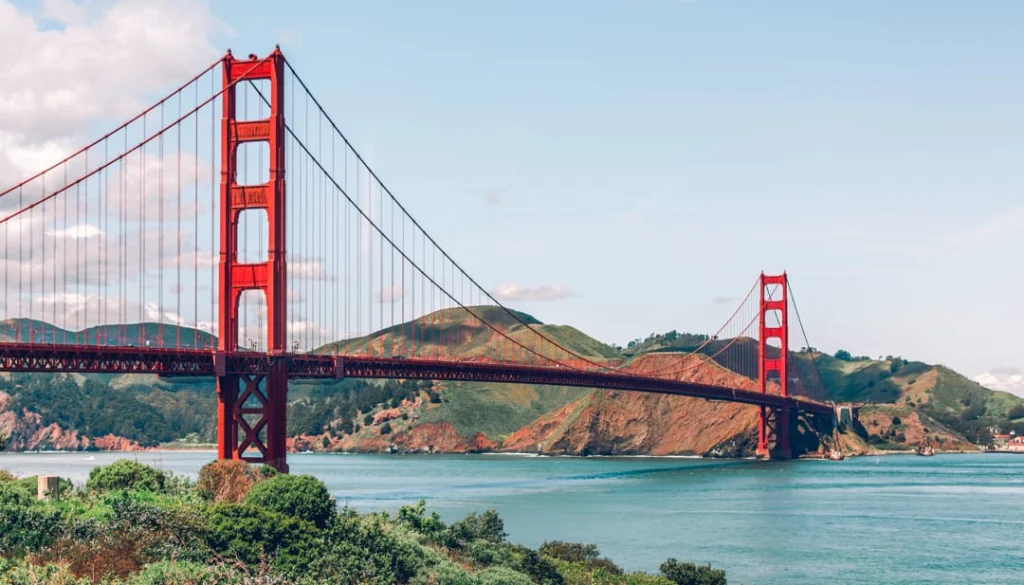 De roodoranje Golden Gate Bridge overspant het blauwe water van de baai met glooiende heuvels op de achtergrond