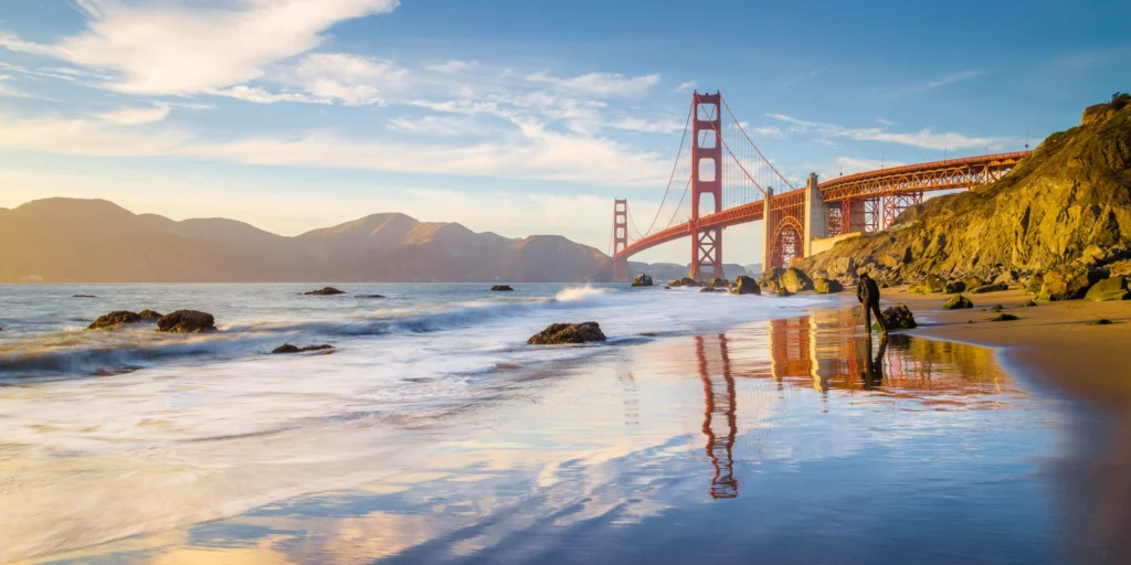 De rode Golden Gate Bridge in San Francisco weerspiegelt in het natte zand terwijl golven op het strand rollen bij zonsondergang