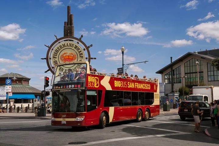 Een rode open dubbeldekker sightseeingbus van Big Bus San Francisco staat bij het stuurwiel van Fisherman's Wharf onder een blauwe hemel