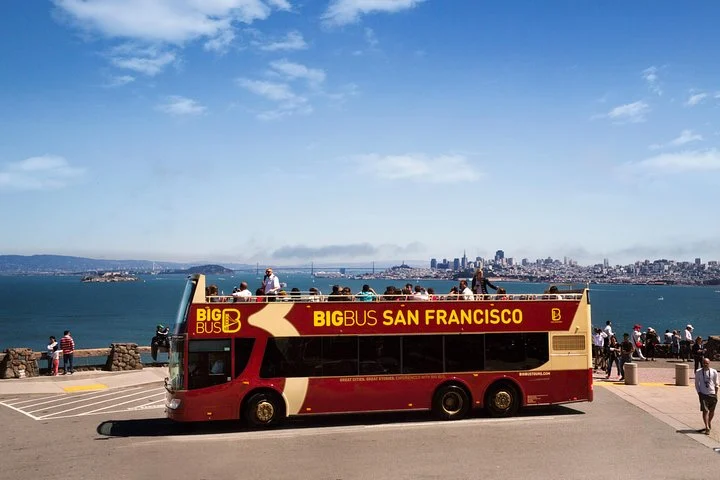Een rode dubbeldekker toeristenbus van Big Bus San Francisco staat geparkeerd op een uitkijkpunt met de skyline en baai van San Francisco op de achtergrond