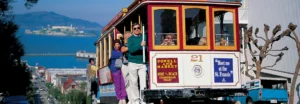 Toeristen op een historische kabeltram in San Francisco met de baai en het eiland Alcatraz op de achtergrond