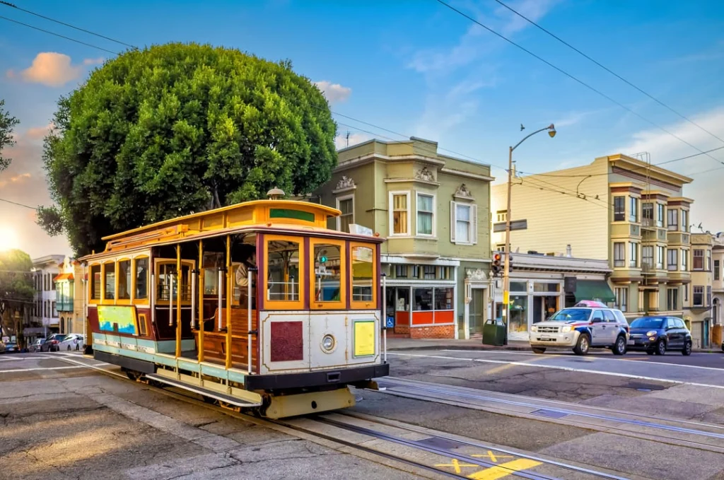 Historische houten kabeltram rijdt over de rails langs winkels en woonhuizen bij zonsondergang in San Francisco