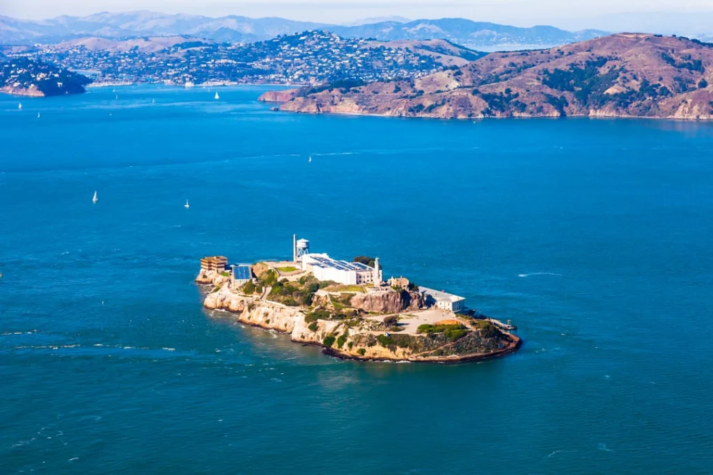Luchtfoto van het rotsachtige gevangeniseiland Alcatraz omringd door blauw water met zeilboten en heuvels op de achtergrond