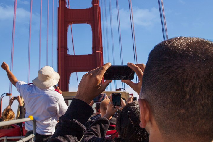 Toeristen op een open dubbeldekker steken hun telefoons omhoog om de rode toren van de Golden Gate Bridge te fotograferen