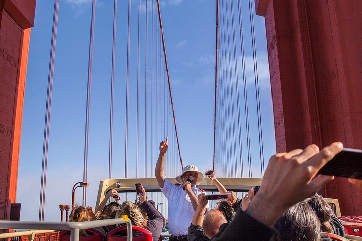 Gids met megafoon steekt zijn vinger omhoog tussen de kabels van de Golden Gate Bridge terwijl toeristen foto's maken