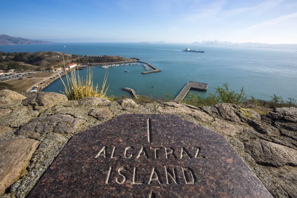 Stenen bord met opschrift Alcatraz Island op de voorgrond met uitzicht over de jachthaven en de baai van San Francisco