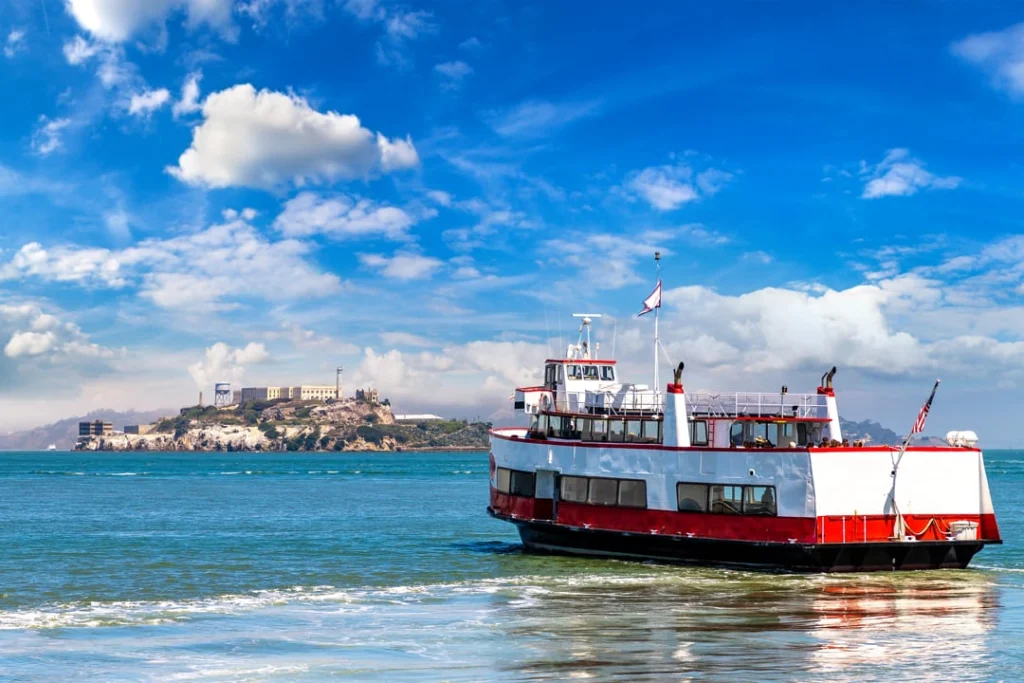 Een rood-witte veerboot vaart over de baai van San Francisco met het eiland Alcatraz op de achtergrond onder een blauwe lucht