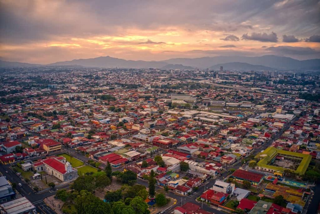 Luchtfoto van de rode daken van San José die zich uitstrekken tot aan de bergen bij een gloeiende zonsondergang