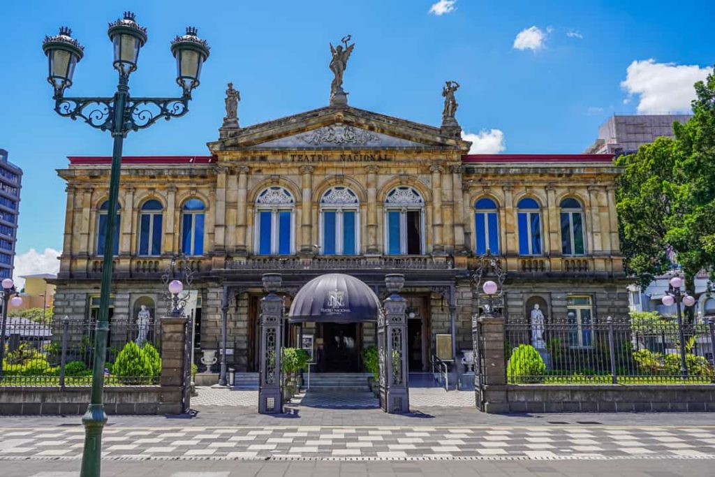 Statige gevel van het Teatro Nacional met standbeelden en sierlijke lantaarnpaal op het plein in San José