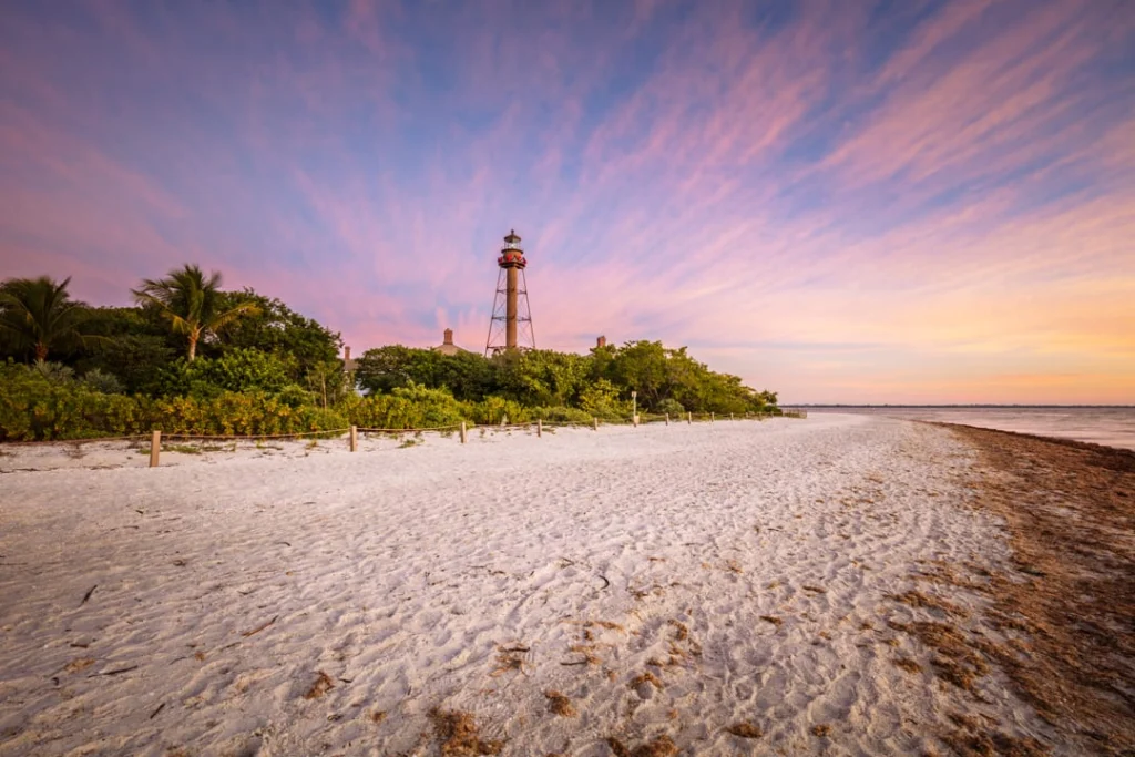 Historische ijzeren vuurtoren van Sanibel Island tussen groene begroeiing op het strand met een roze gekleurde avondlucht