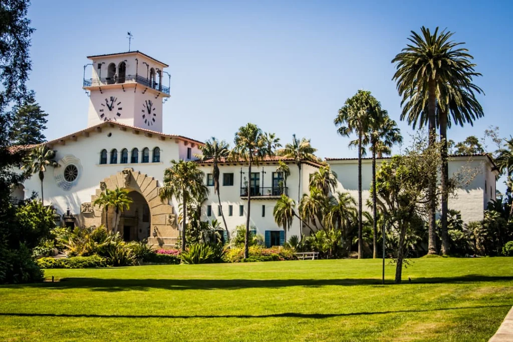 Wit gebouw in Spaans koloniale stijl met een klokkentoren en rode dakpannen, omgeven door palmbomen en een groen gazon in Santa Barbara