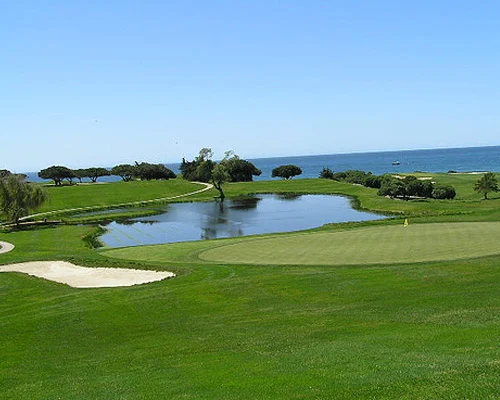 Groene golfbaan met een waterhindernis en bomen loopt af naar de oceaan onder een strakblauwe hemel bij Santa Barbara