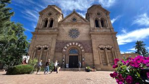 Romaanse zandstenen kathedraal met twee torens en een roosvenster, met bezoekers en bloeiende bougainville op de voorgrond in Santa Fe