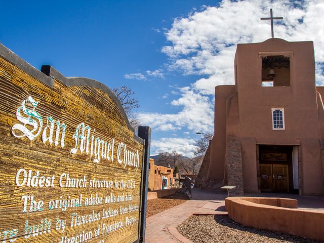 Bruine adobe kerktoren van San Miguel Church in Santa Fe met een bord ervoor dat vertelt dat het het oudste kerkgebouw van de Verenigde Staten is