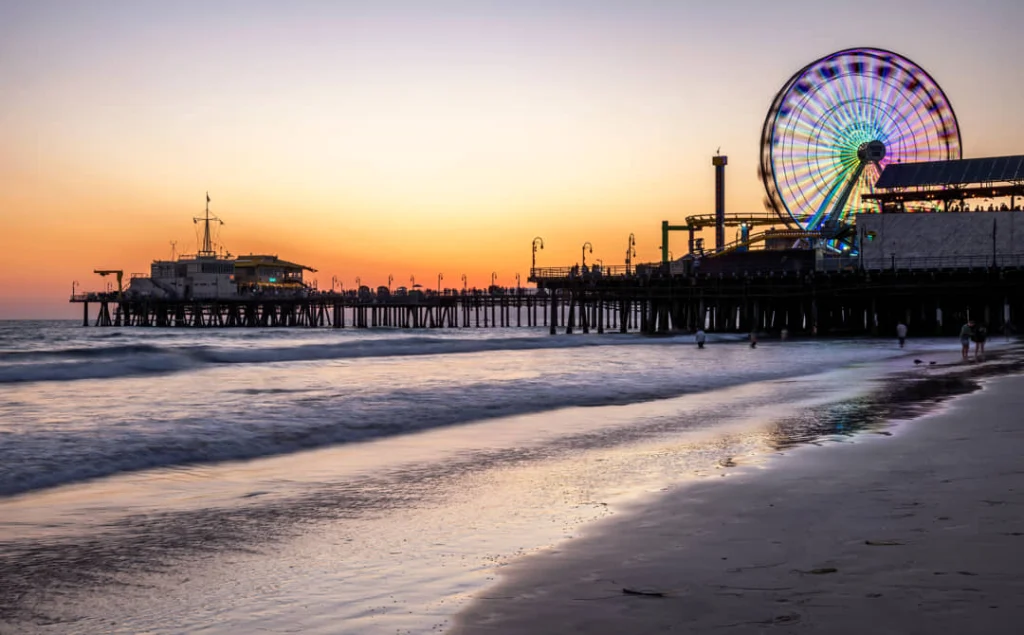Verlicht reuzenrad op de pier van Santa Monica met mensen op het strand tijdens een gekleurde zonsondergang
