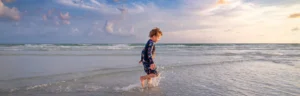 Een jongen in een zwempak rent door de ondiepe golven op het strand van Sarasota bij zonsondergang