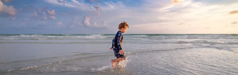 Een jongen in een zwempak rent door de ondiepe golven op het strand van Sarasota bij zonsondergang