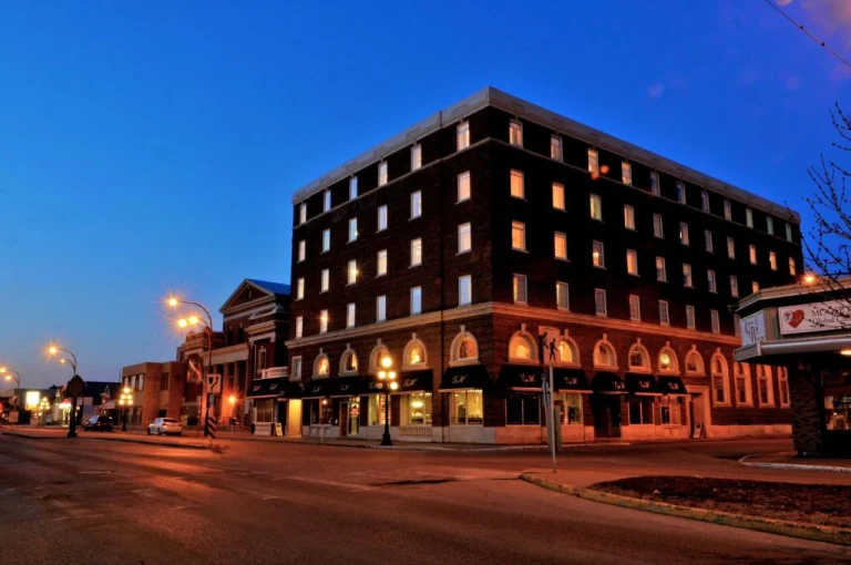 Bakstenen hotelgebouw van meerdere verdiepingen op een straathoek in Saskatchewan, verlicht bij het vallen van de avond met een lege straat ervoor