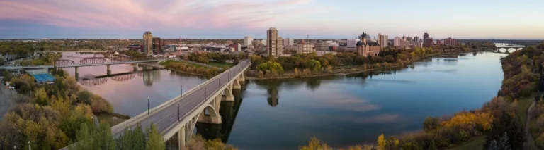 Breed panorama van Saskatoon bij zonsondergang met een boogbrug over de South Saskatchewan River en de skyline op de achtergrond