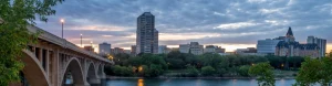 Panorama van Saskatoon in de avondschemering met een gewelfde brug over de South Saskatchewan River en verlichte gebouwen op de achtergrond