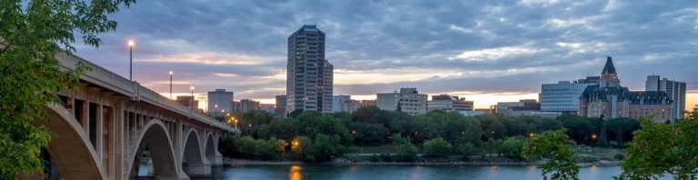 Panorama van Saskatoon in de avondschemering met een gewelfde brug over de South Saskatchewan River en verlichte gebouwen op de achtergrond