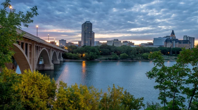 Silhouet van de skyline van Saskatoon in de avondschemering met een stenen boogbrug over de South Saskatchewan River en bomen op de voorgrond