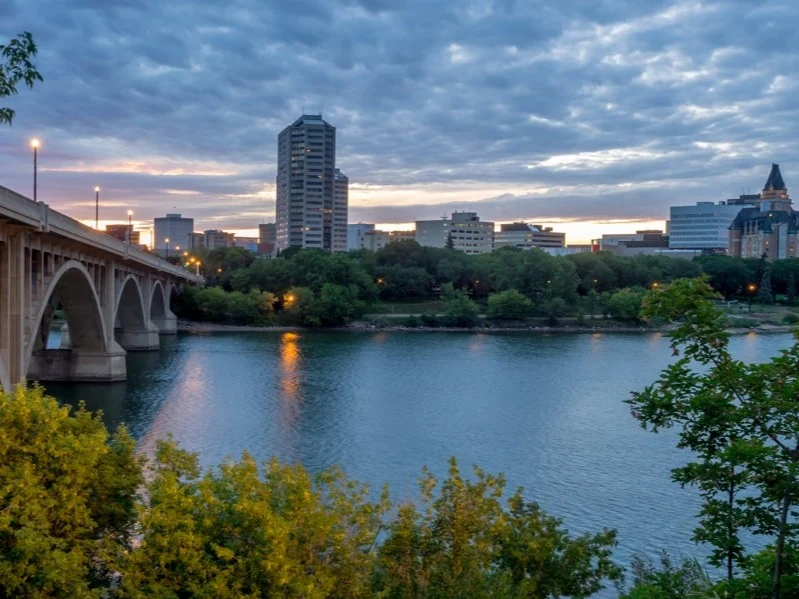 Boogbrug over de South Saskatchewan River met de skyline van Saskatoon op de achtergrond bij een warme zonsondergang