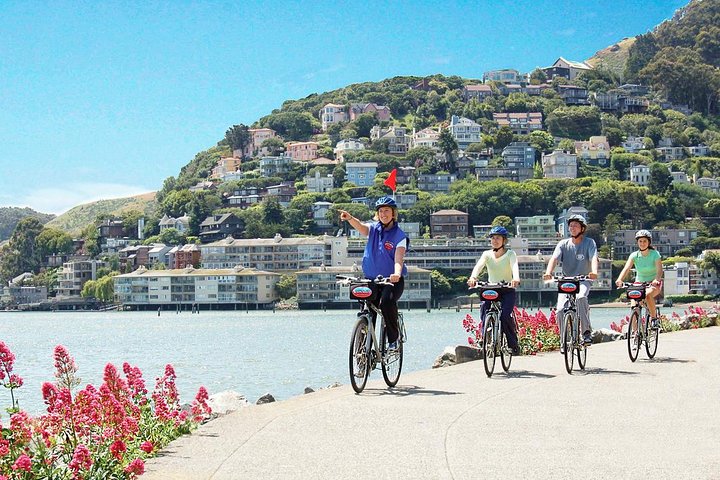 Groep fietsers rijdt langs het water met op de achtergrond een heuvel vol kleurrijke huizen in Sausalito