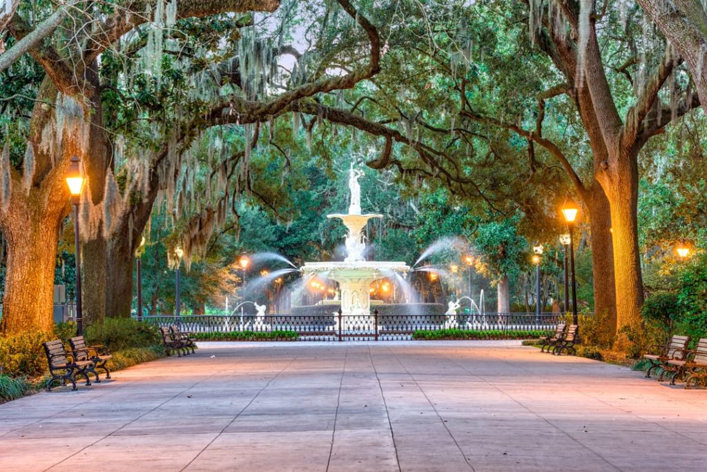 Verlichte sierfontein aan het einde van een laan met oude eikenbomen en hangend Spaans mos in Forsyth Park in Savannah in Georgia bij avondlicht