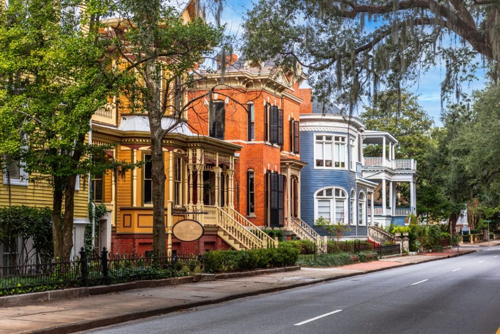 Rij sierlijke Victoriaanse huizen in geel, rood en blauw met erkers en verandas langs een straat met bomen in Savannah in Georgia