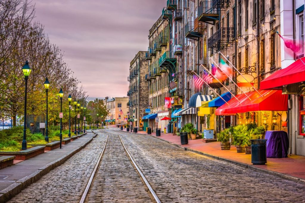 Bestrate straat met oude rails langs historische bakstenen gebouwen met gestreepte luifels en vlaggen op River Street in Savannah in Georgia