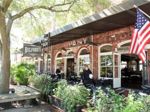 Buitenterras met tafels onder een luifel en een grote Amerikaanse vlag bij restaurant Belford's in een bakstenen pand in Savannah in Georgia