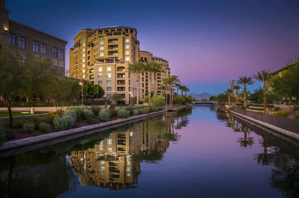 Rustig kanaal met palmbomen en verlichte appartementengebouwen die weerspiegelen in het water bij schemering in Scottsdale