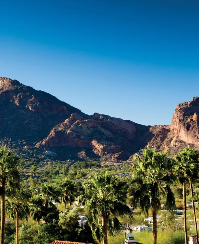 Rossige, kartelige bergketen die uitrijst boven een groene vallei met palmbomen en woningen in Scottsdale