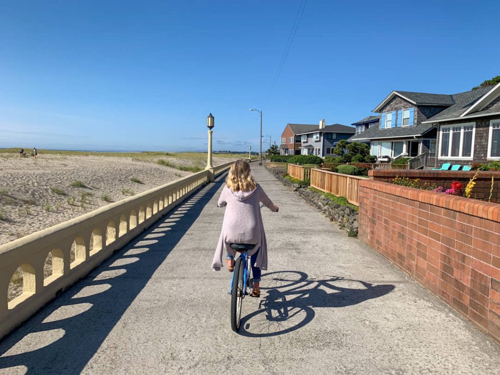 Meisje fietst over een betonnen promenade met een sierlijke balustrade, huizen aan de ene kant en het strand aan de andere kant in Seaside