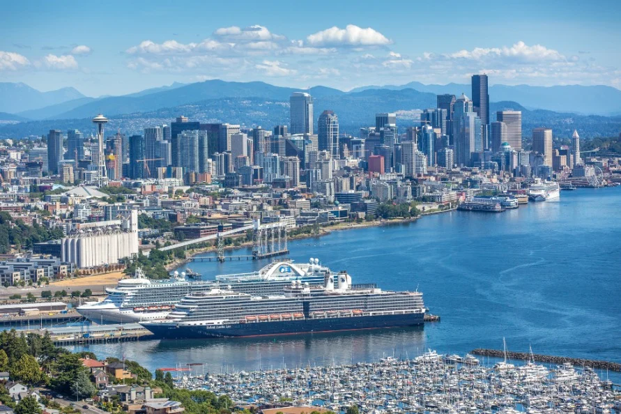 Luchtfoto van de skyline van Seattle met wolkenkrabbers, de Space Needle en een groot cruiseschip afgemeerd aan de waterkant met een jachthaven ervoor
